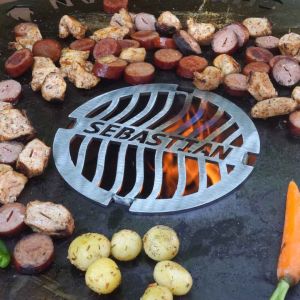 Wurst und Fleisch grillt neben Grillrost Ø 21 mit Wunschname auf Feuerplatte von Schamotte-Shop.de