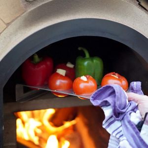 Tomaten Paprika Halter aus Edelstahl wird mit gefüllten Tomaten und Paprika in Steinofen geschoben