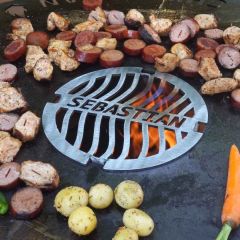 Wurst und Fleisch grillt neben Grillrost Ø 21 mit Wunschname auf Feuerplatte von Schamotte-Shop.de