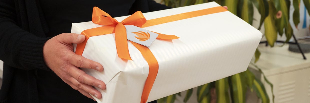 Weißes Geschenk mit orangenem Geschenkband in der Hand