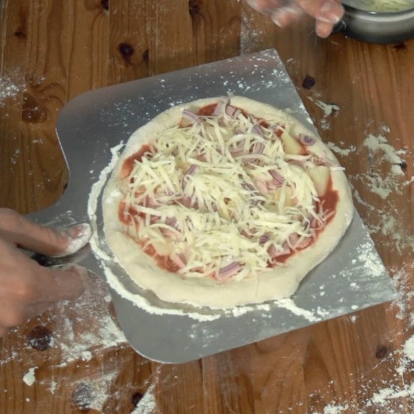 Pizzaschieber mit Pizza Hawaii vor Backen auf dem Pizzastein