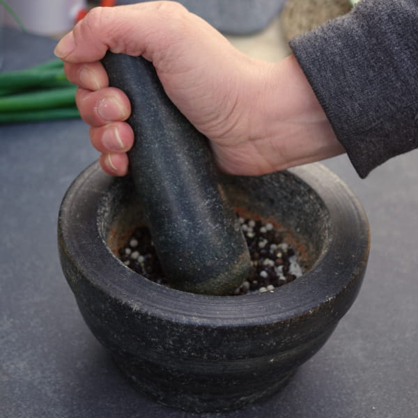 Pfefferkörner mit Stösel im Mörser mahlen